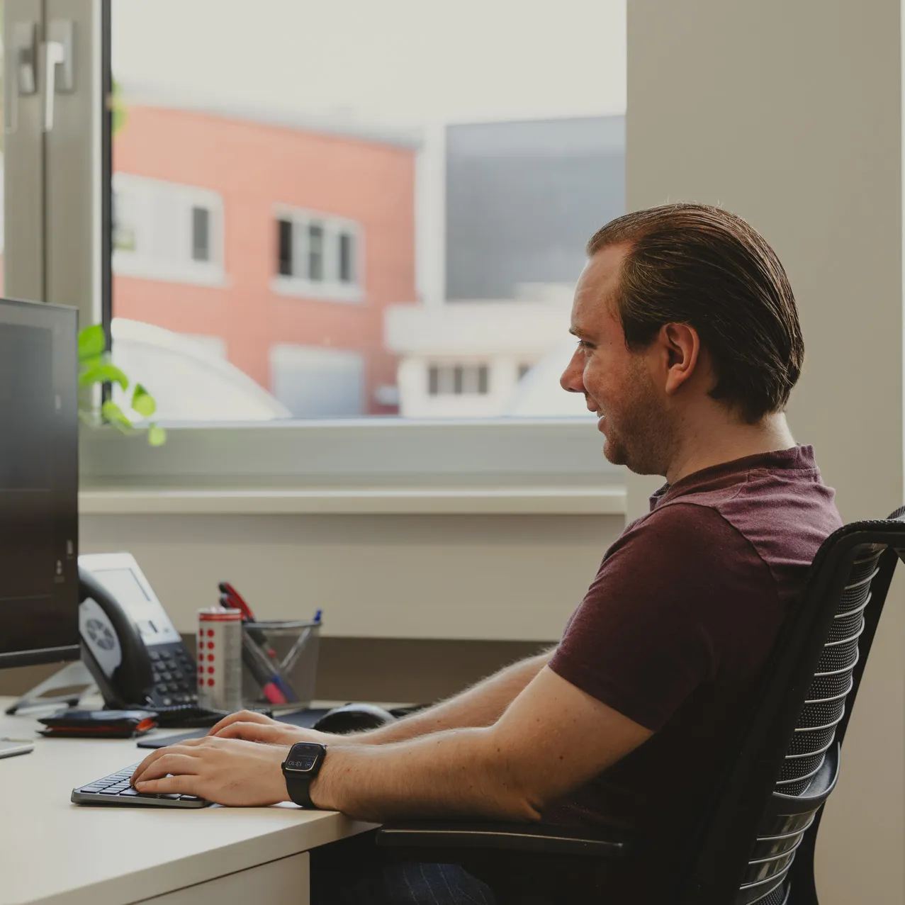 One employee sitting at his desk in front of his computer laughing photographed from the side