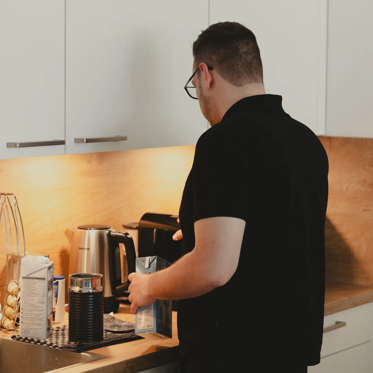 Another employee in the office kitchen preparing his coffee photographed from behind