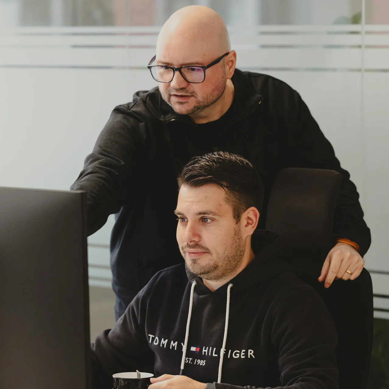 Two employees looking at one screen discussing a topic photographed from the front
